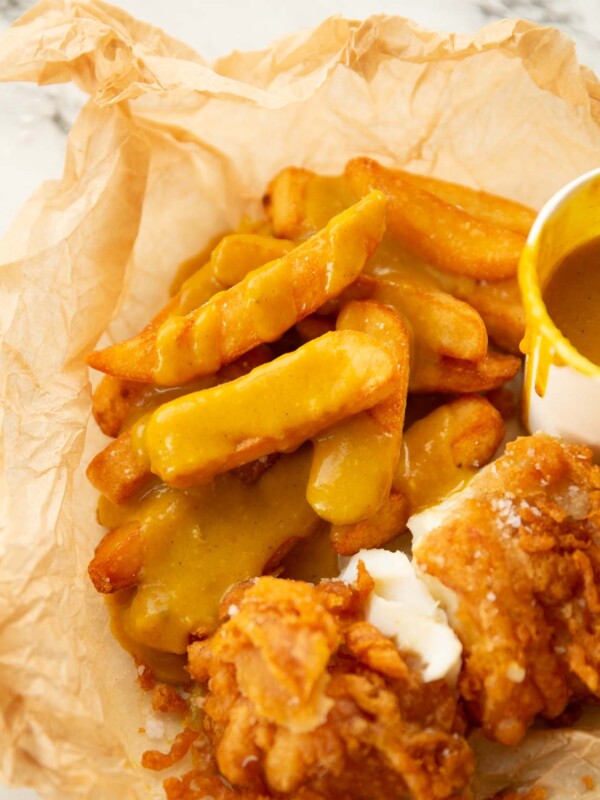 fish and chips covered in curry sauce in scrunched up baking paper