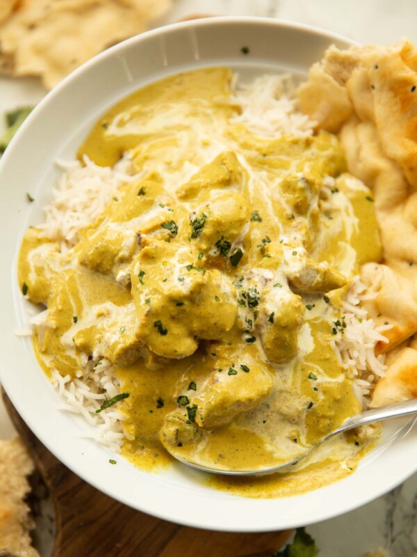 close up shot of chicken korma in large white dish on rice with naan bread