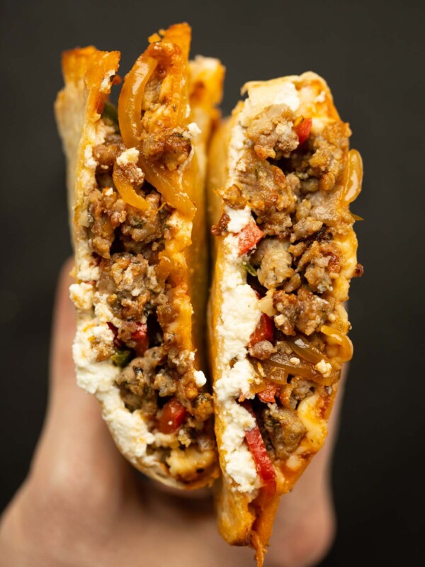 close up overhead shot of hand holding sausage peppers tortilla calzone sliced open