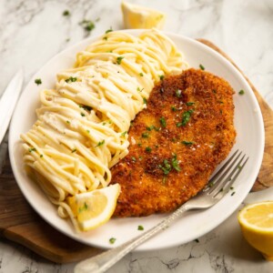 creamy lemon chicken pasta served on small white plate on wooden chopping board