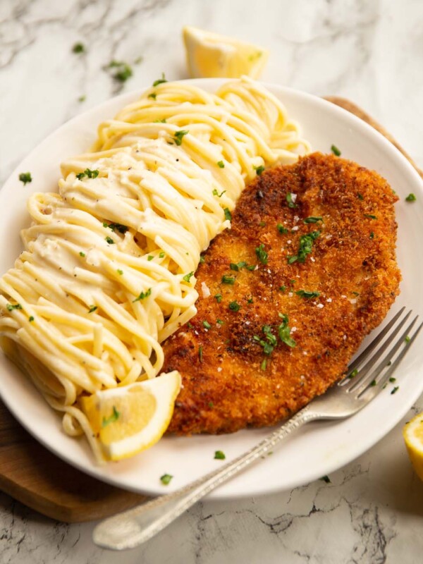 creamy lemon chicken pasta served on small white plate on wooden chopping board