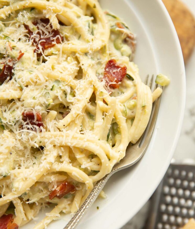 close up shot of courgette bacon pasta in white dish with silver fork