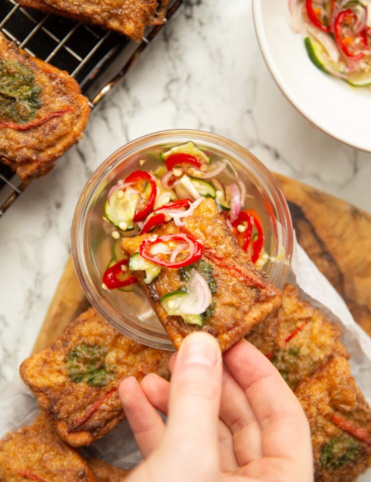 hand dunking thai pork toast into pot of dipping sauce