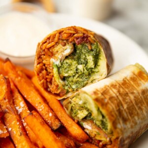 halved chicken pesto wrap on white plate with sweet potato fries