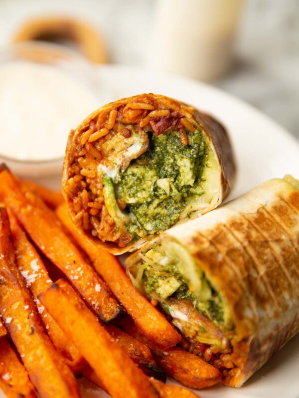 halved chicken pesto wrap on white plate with sweet potato fries