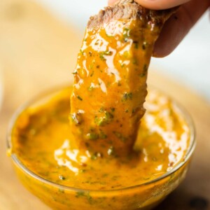 close up shot of hand dunking slice of steak into small pot of cowboy butter