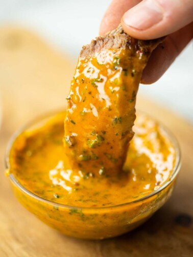 close up shot of hand dunking slice of steak into small pot of cowboy butter