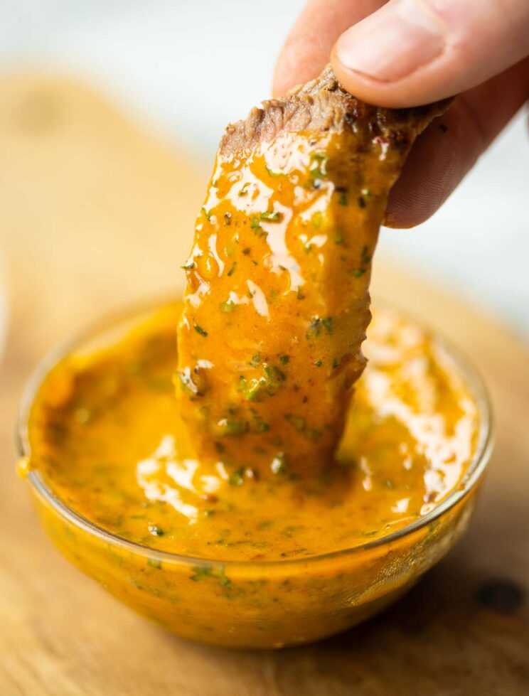 close up shot of hand dunking slice of steak into small pot of cowboy butter