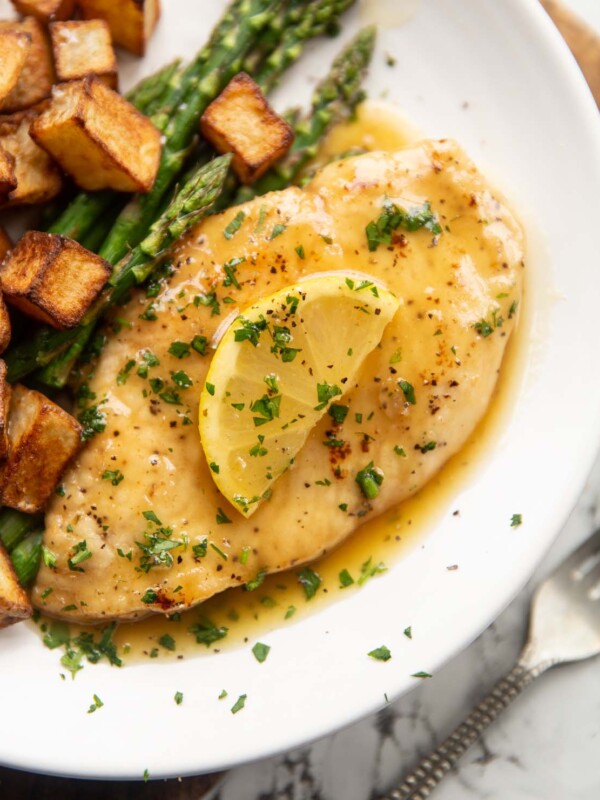 honey lemon chicken breast on small white plate with asparagus and roast potatoes