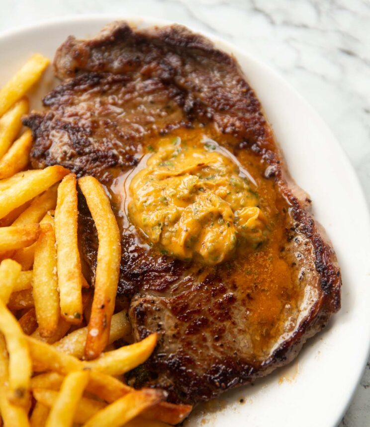 close up shot of steak and cowboy butter with fries on small white plate