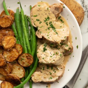 overhead shot of sliced pork tenderloin with boursin sauce on white plate with potatoes and green beans