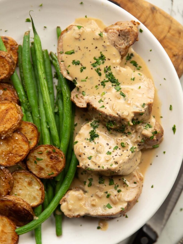 overhead shot of sliced pork tenderloin with boursin sauce on white plate with potatoes and green beans