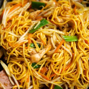 chicken chow mein in large wok with wooden spoons at the side