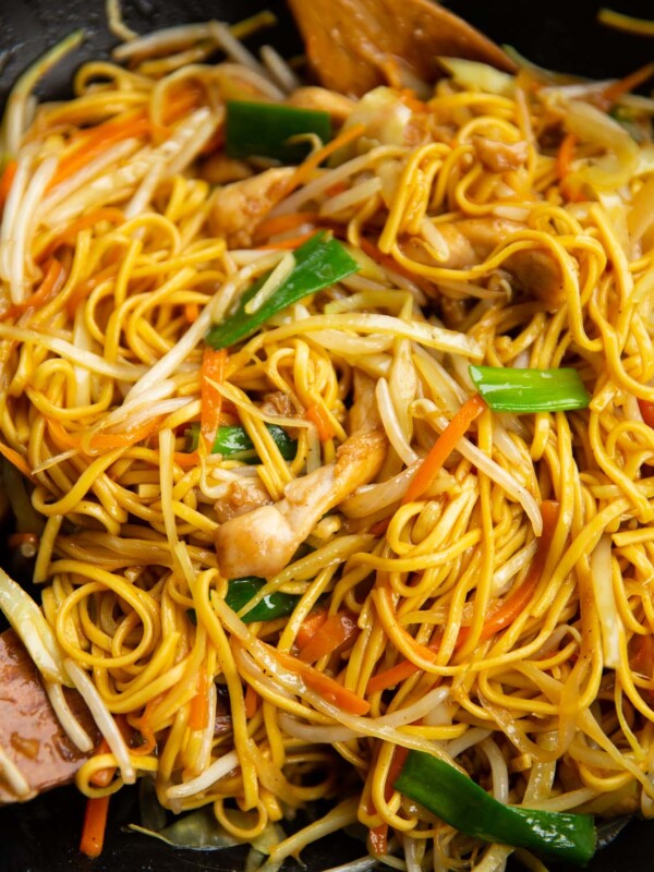 chicken chow mein in large wok with wooden spoons at the side