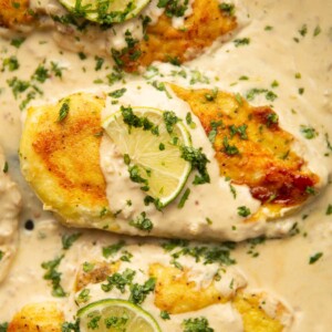 overhead close up shot of 3 creamy coconut lime chicken breasts in pan garnished with lime and coriander