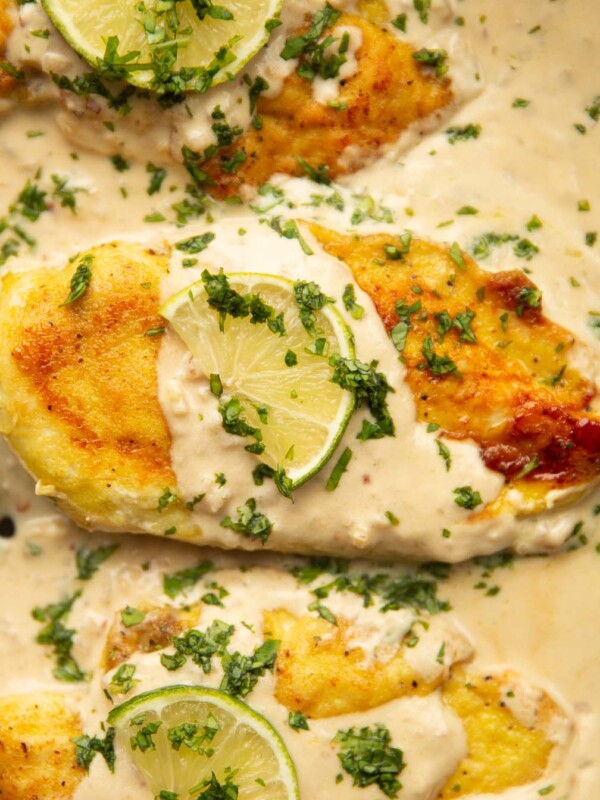 overhead close up shot of 3 creamy coconut lime chicken breasts in pan garnished with lime and coriander