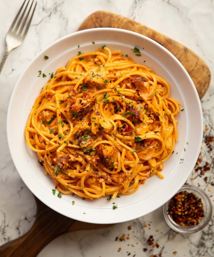 overhead shot of creamy tomato salmon pasta in large white bowl on wooden chopping board