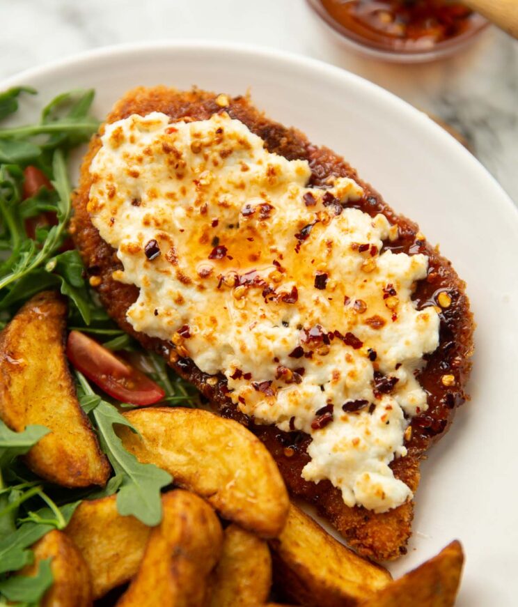 close up shot of crispy hot honey feta chicken on white plate with wedges and rocket