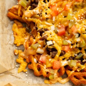 close up shot of loaded cheeseburger waffle fries on baking paper