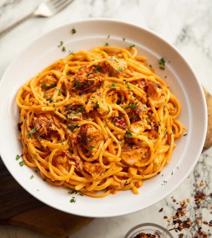 spicy salmon pasta served in large white bowl on marble backdrop