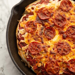 tortilla pizza in large cast iron pan on marble backdrop