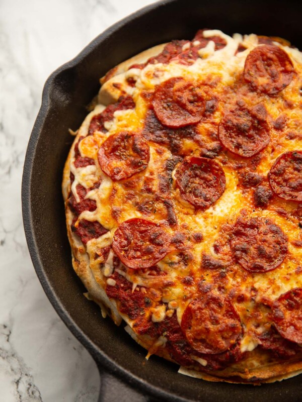 tortilla pizza in large cast iron pan on marble backdrop