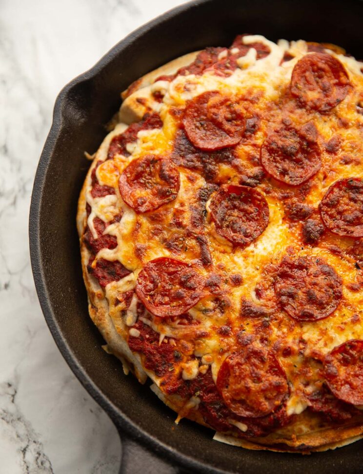 tortilla pizza in large cast iron pan on marble backdrop