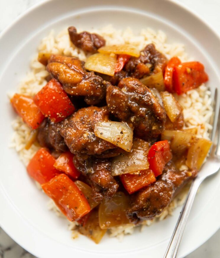 close up overhead shot of black pepper chicken on rice in large white bowl