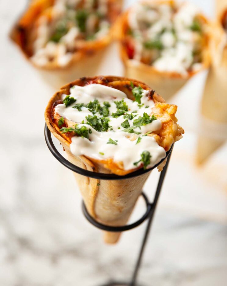 chicken quesadilla cone in ice cream holder topped with sour cream and coriander