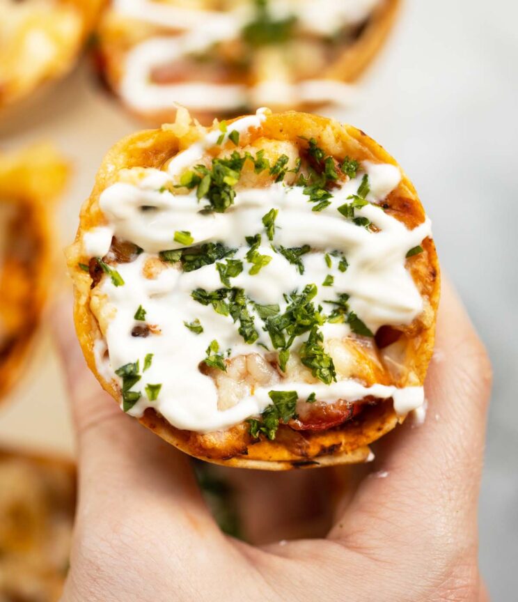 close up overhead shot of hand holding chicken quesadilla cone topped with sour cream and coriander