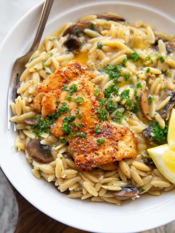 garlic butter chicken orzo served in large white bowl with fork and lemon wedges