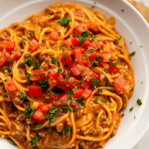 close up shot of taco spaghetti in large white dish with tomatoes and coriander