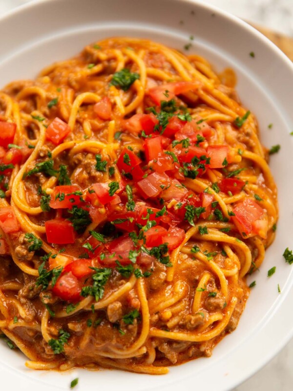 close up shot of taco spaghetti in large white dish with tomatoes and coriander