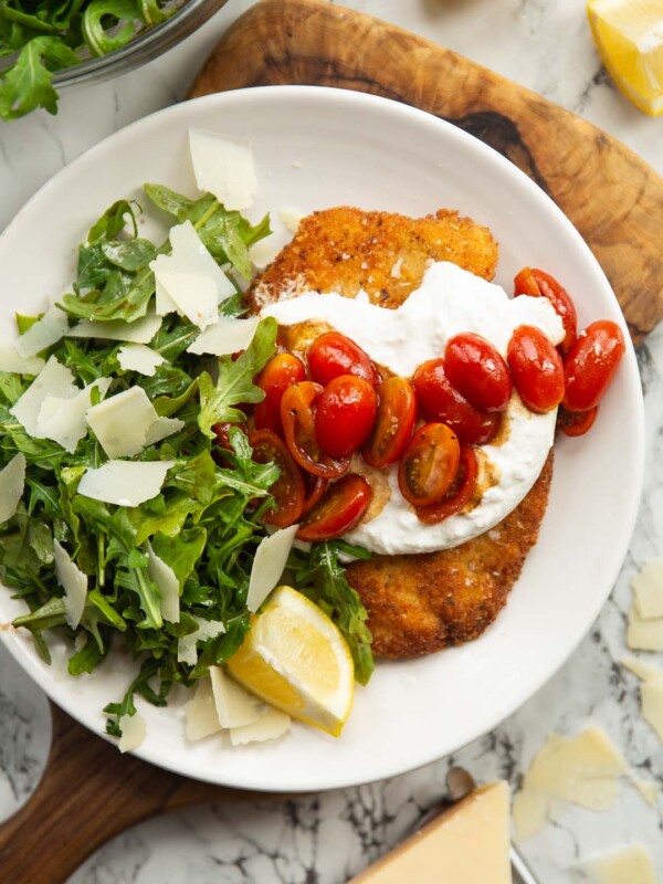 overhead shot of chicken milanese burrata on small white plate on wooden chopping board