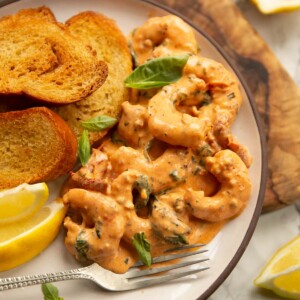 creamy tuscan style prawns served on small white plate with toasted bread and lemon wedges