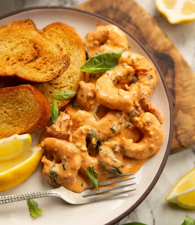 creamy tuscan style prawns served on small white plate with toasted bread and lemon wedges