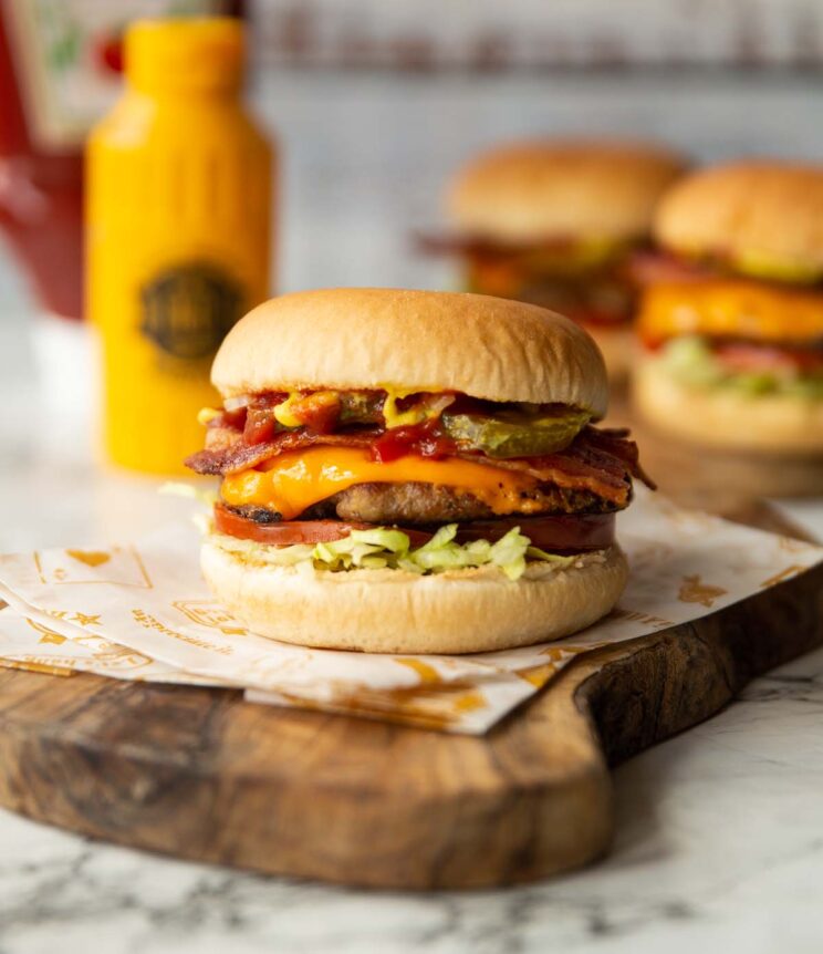 sausage smash burger on wooden board with condiments in background