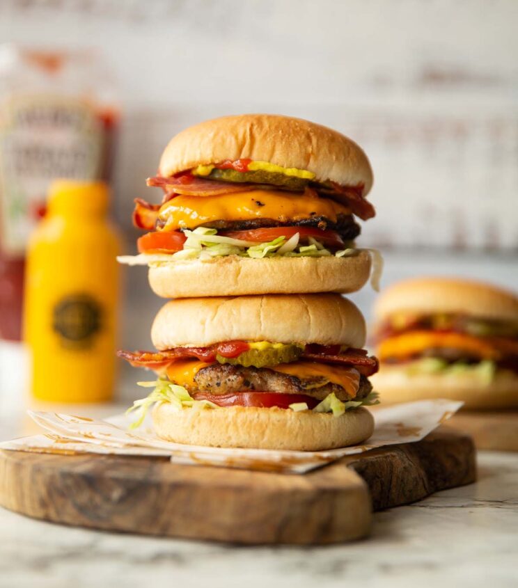 2 sausage smash burgers stacked on each other on wooden chopping board