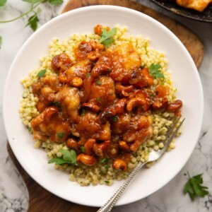 overhead shot of sticky apricot chicken on cous cous on small white plate with silver fork