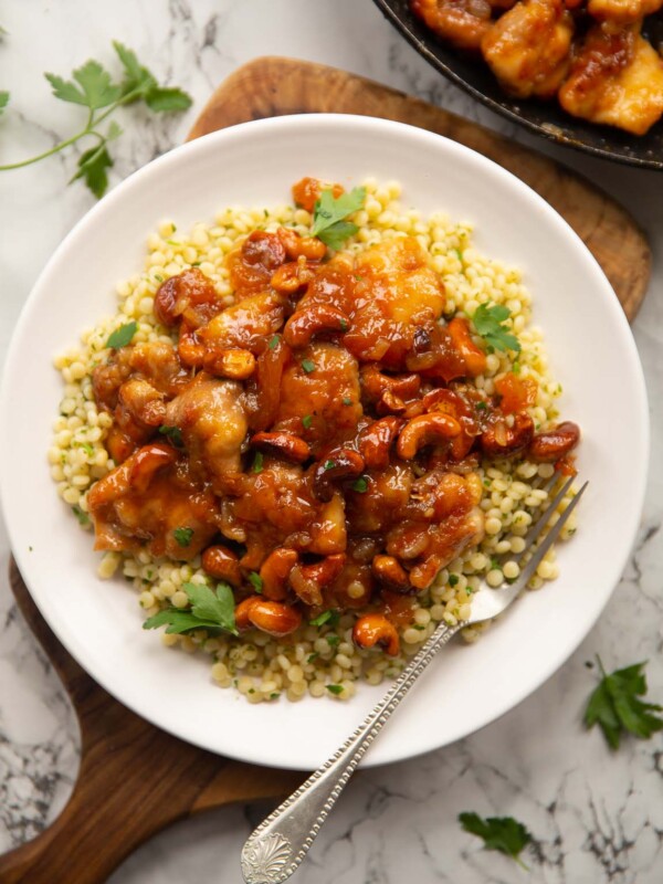 overhead shot of sticky apricot chicken on cous cous on small white plate with silver fork