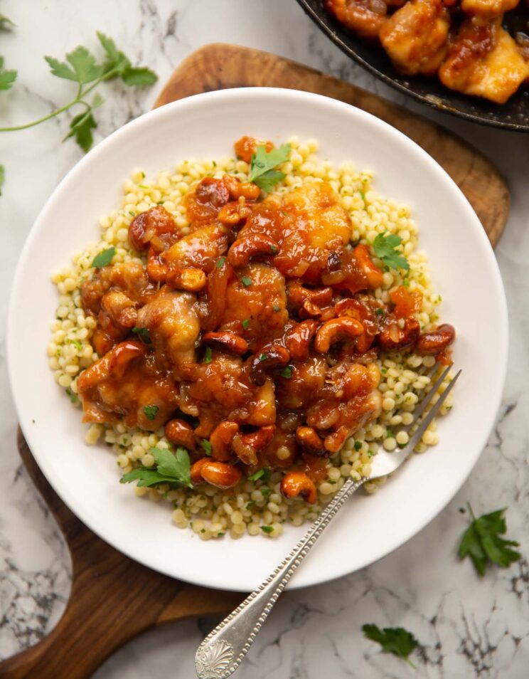 overhead shot of sticky apricot chicken on cous cous on small white plate with silver fork