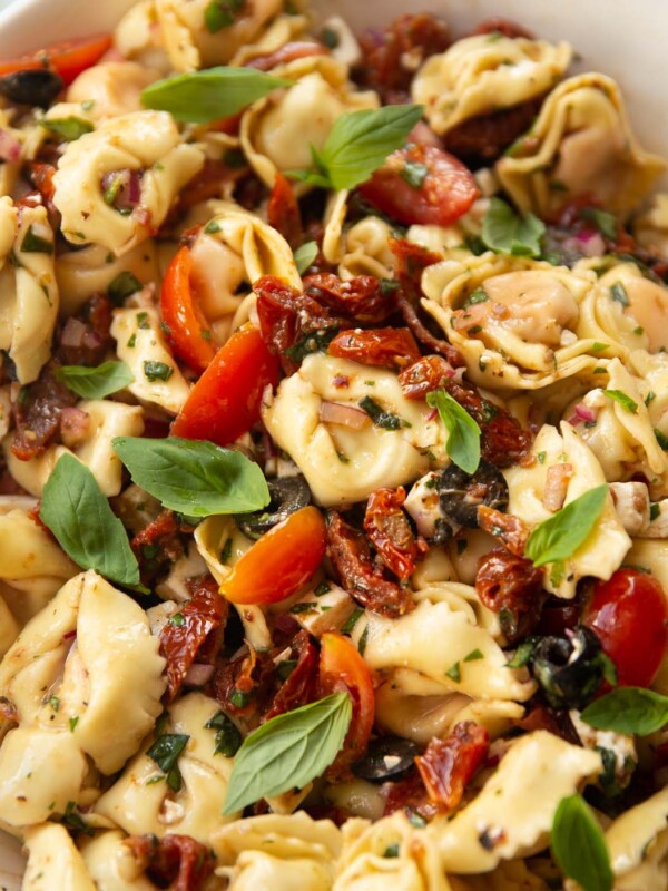 Sun dried tomato tortellini pasta salad in a large white bowl garnished with basil