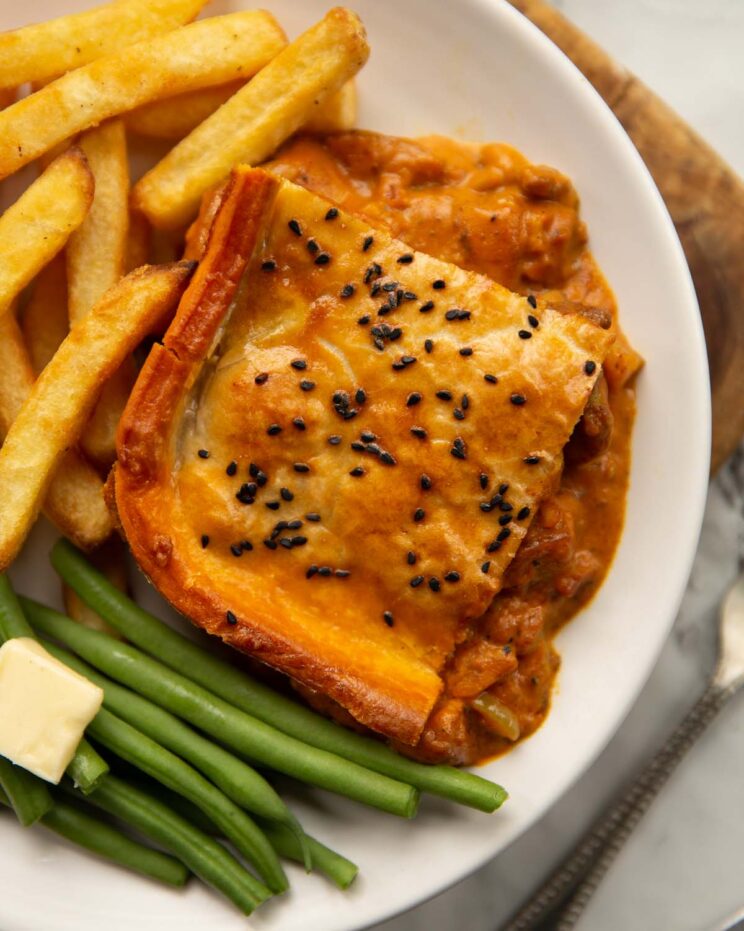 overhead shot of chicken curry pie on small white plate with chips and green beans