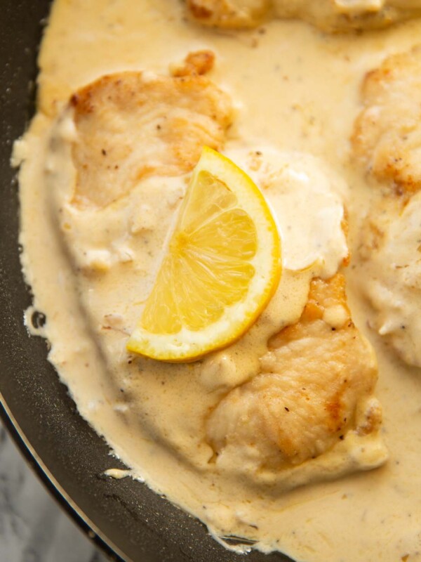 close up shot of creamy lemon chicken in pan with lemon wedge on top