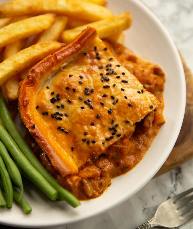 curry chicken pie on small white plate with chips and green beans