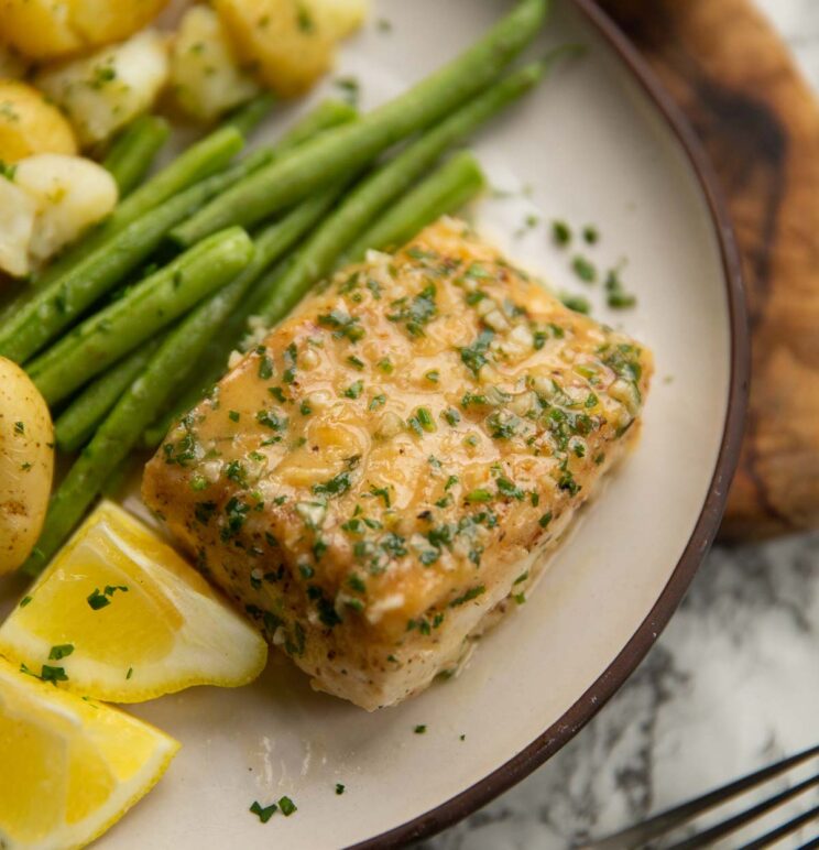 garlic butter cod served on small white plate with green beans, lemon wedges and baby potatoes