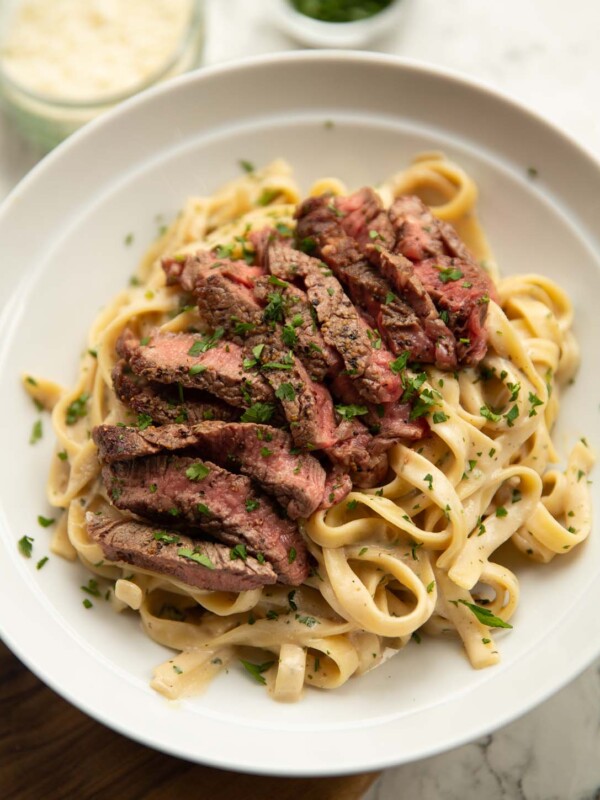 boursin steak pasta served in white bowl with pot of parsley and parmesan in background