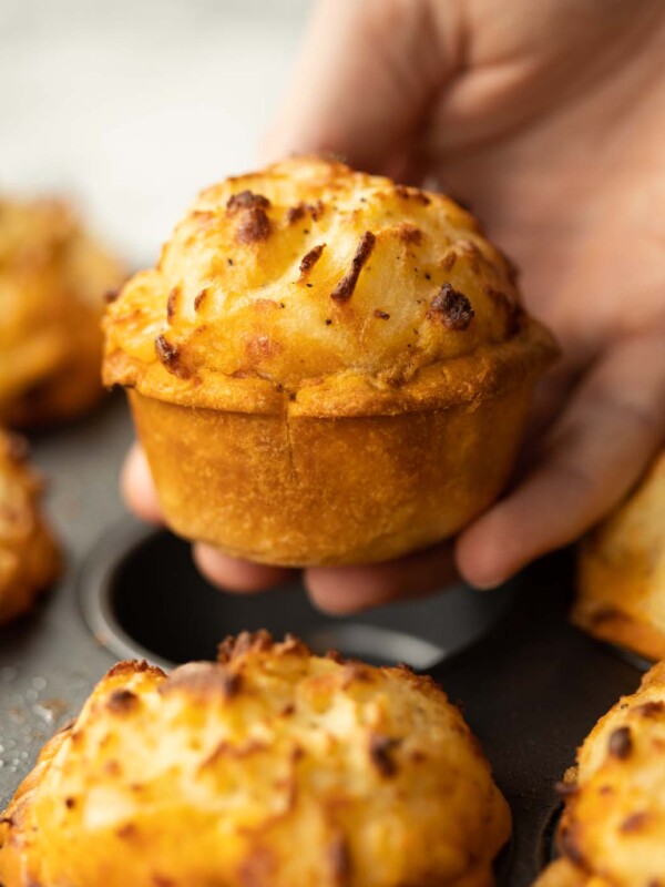 close up shot of hand holding mini cottage pie above muffin tin