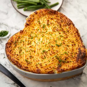 classic fish pie served in heart shaped baking dish with green beans in background