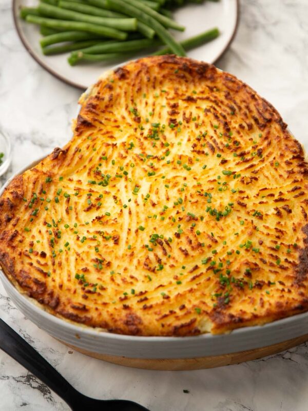 classic fish pie served in heart shaped baking dish with green beans in background